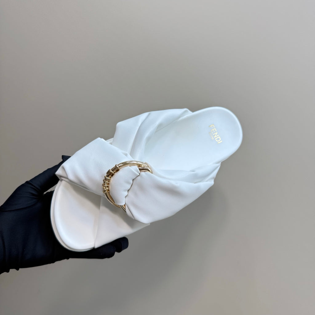 White Fendi slide sandal with gold chain buckle, held in gloved hand