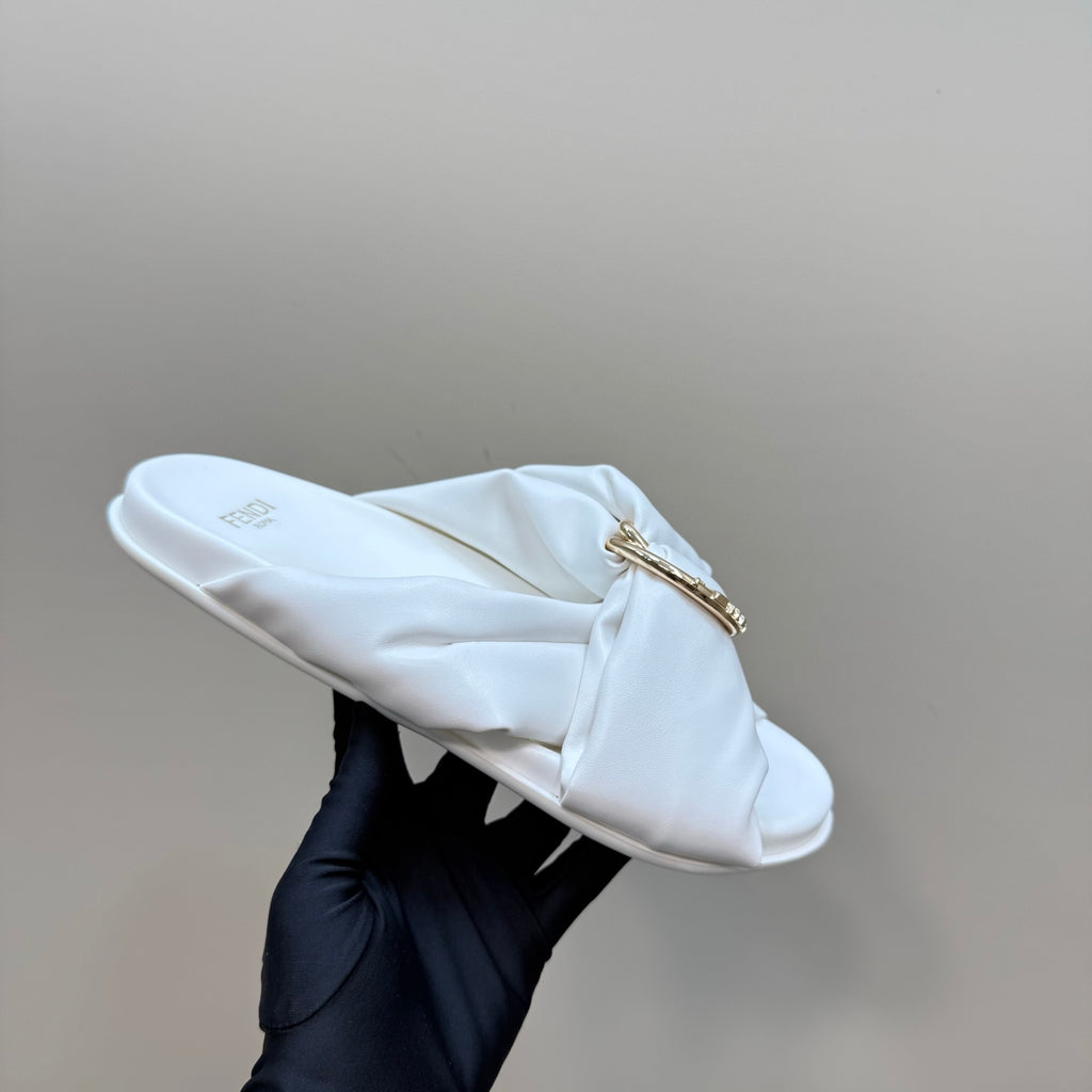 White Fendi slide sandal with gold chain detail, held in a gloved hand