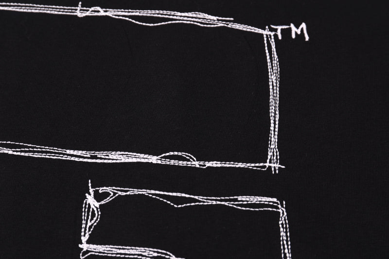 Black T-shirt back graphic close-up: outlined rectangles and lines with TM mark