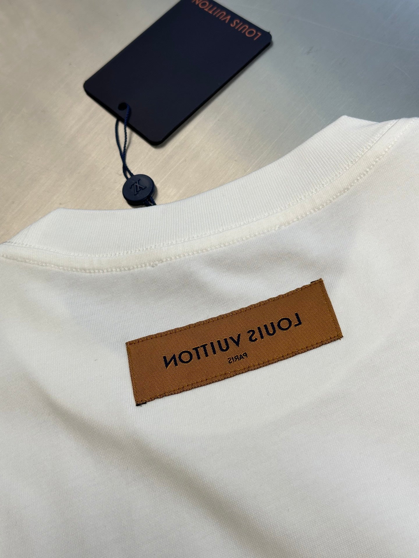 White T-shirt hem with Louis Vuitton brown label and navy hang tag