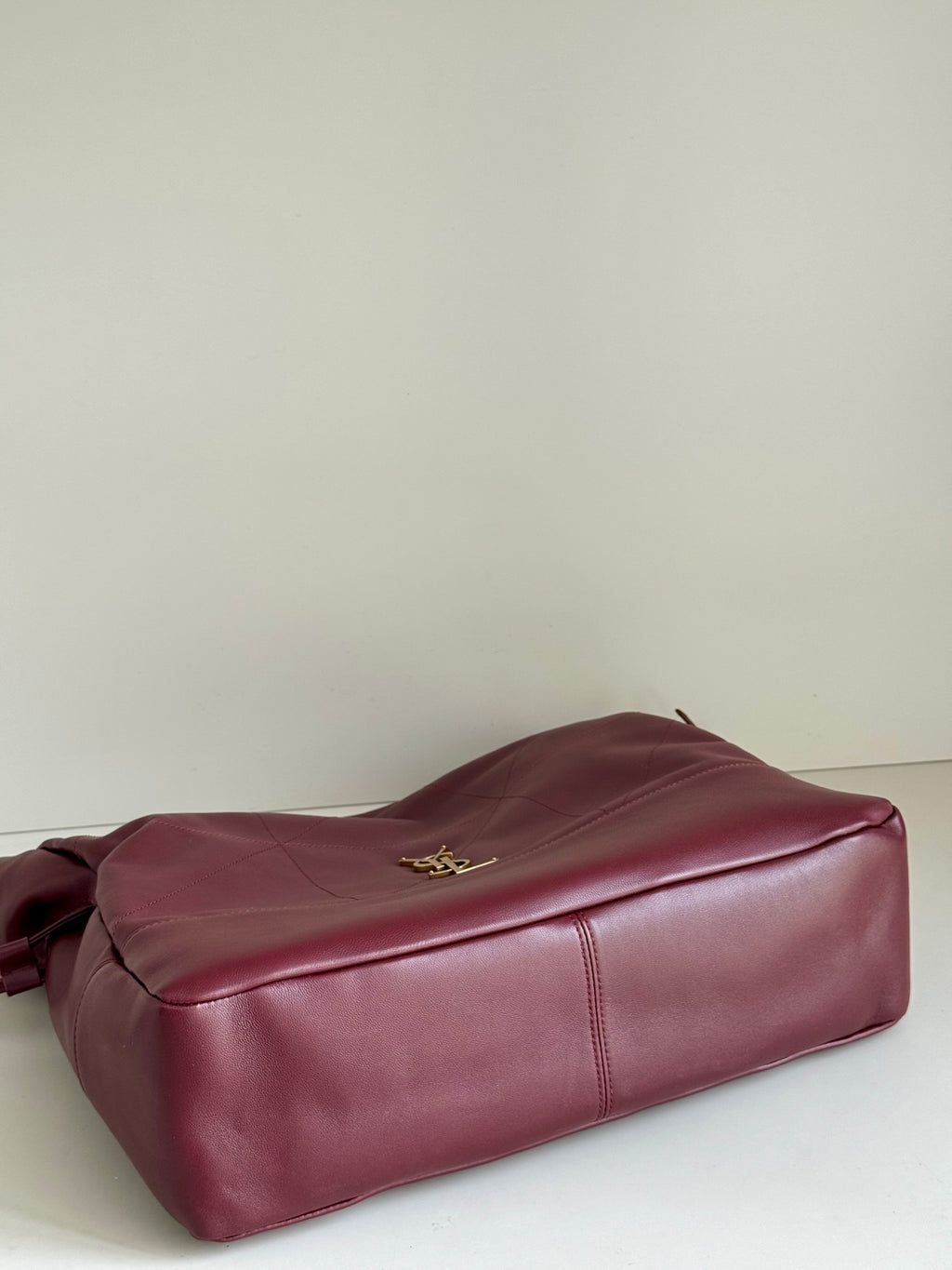 YSL leather tote bag in burgundy laid on side with gold logo on top panel