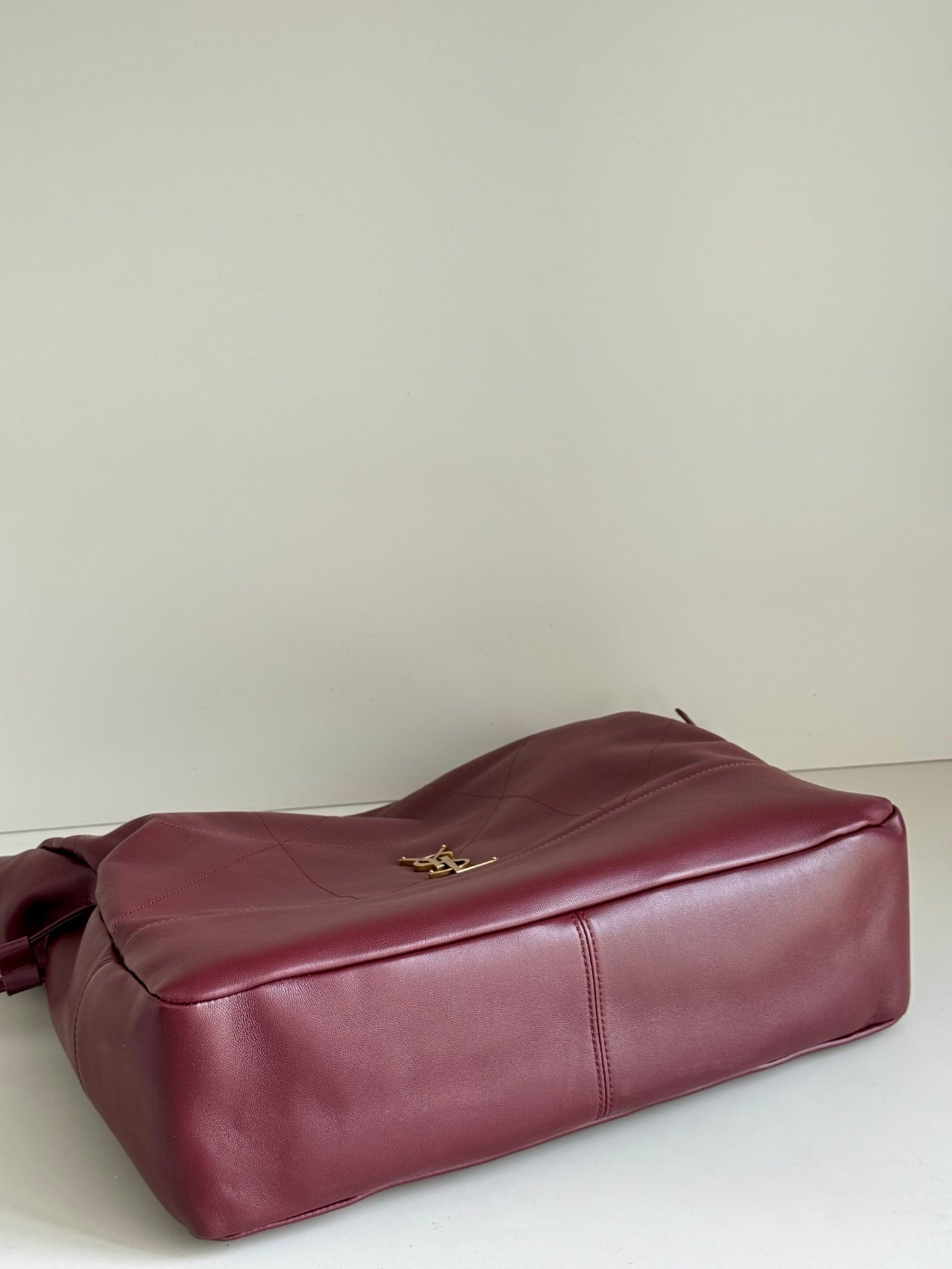 YSL leather tote bag in burgundy laid on side with gold logo on top panel