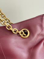 YSL tote bag close-up with gold chain and circular logo plate on burgundy leather