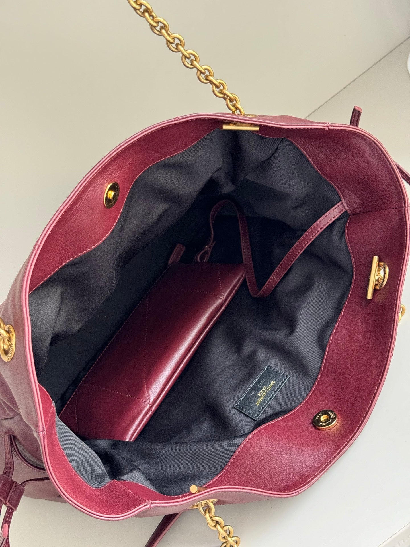 YSL burgundy tote bag interior with navy lining, open top, and gold hardware accents
