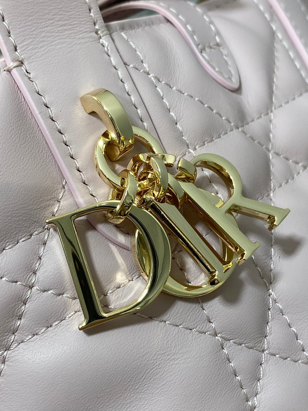 Dior charm hardware on pink quilted handbag, gold-toned letters and clips