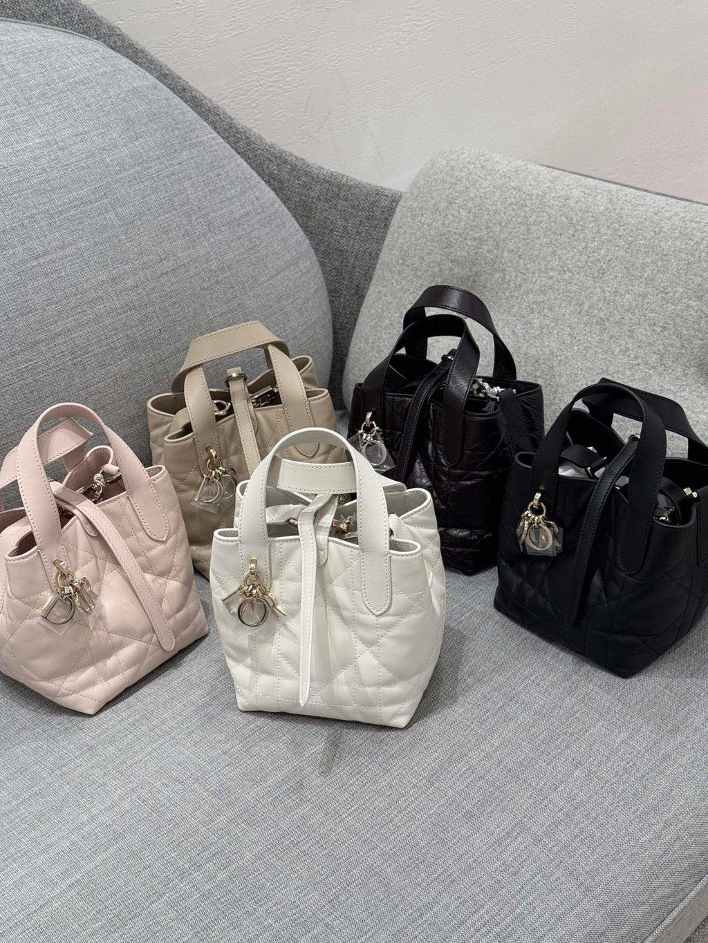 Dior bag mini totes on display: light pink, white, beige, and black with charms