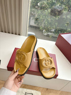 Gold Gucci slide sandals held in hand with interlocking G strap detail