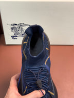 Burberry blue knit sneaker held by hand, showing eyelet laces and yellow trim
