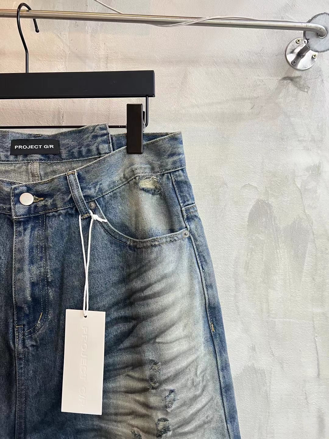 Blue denim shorts side view with frayed hem, drawstring detail and hanging tag