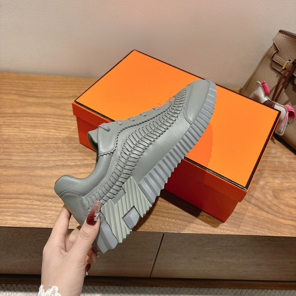 Gray sneakers held by hand, showing side stripes and deep tread on sole.