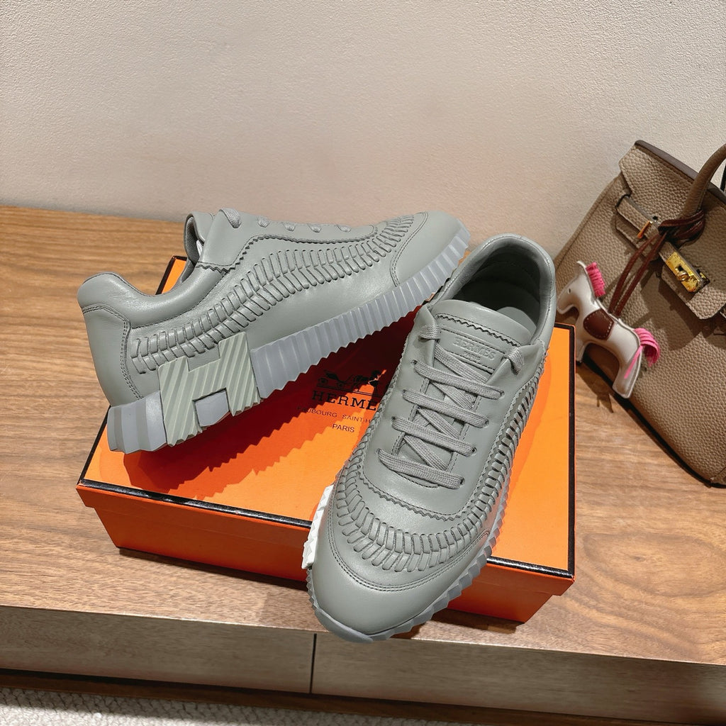 Gray lace-up sneakers with textured strap-like seams and thick treaded sole.