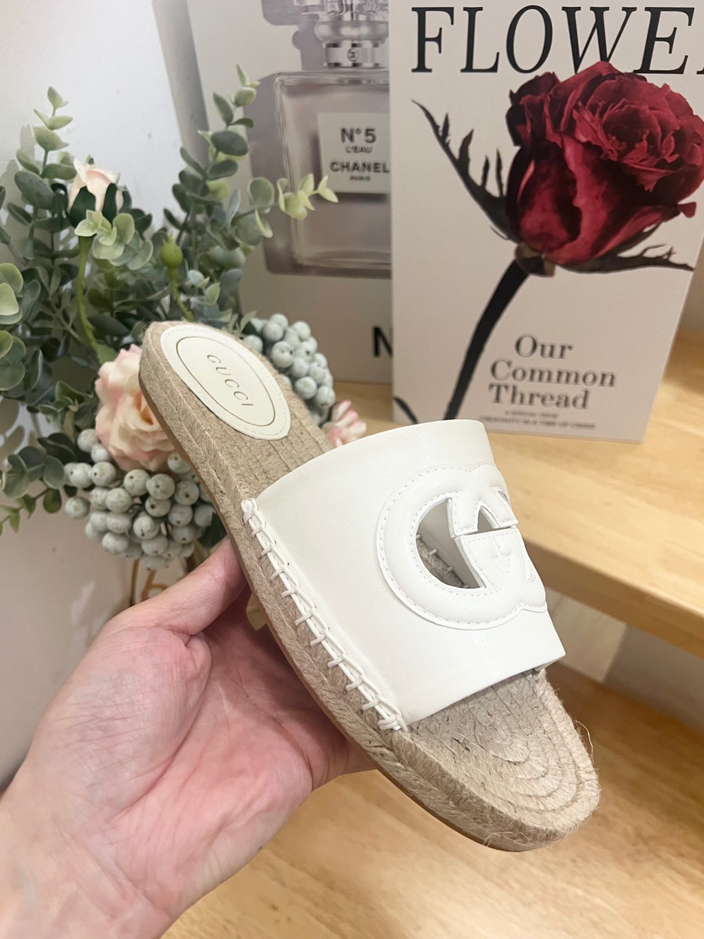 Gucci white slide sandal with cutout logo strap and woven jute sole, held up.