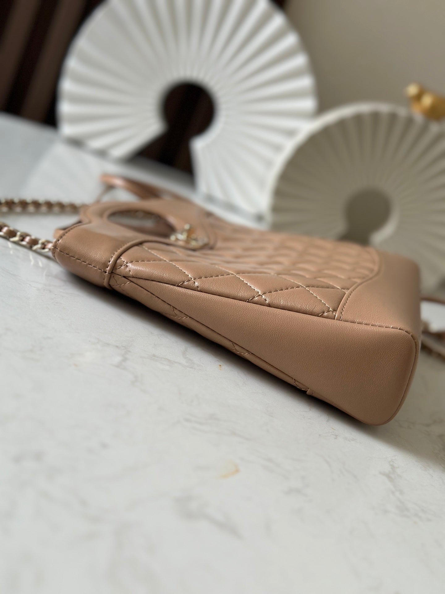 Chanel quilted beige handbag angled view with chain strap and curved base