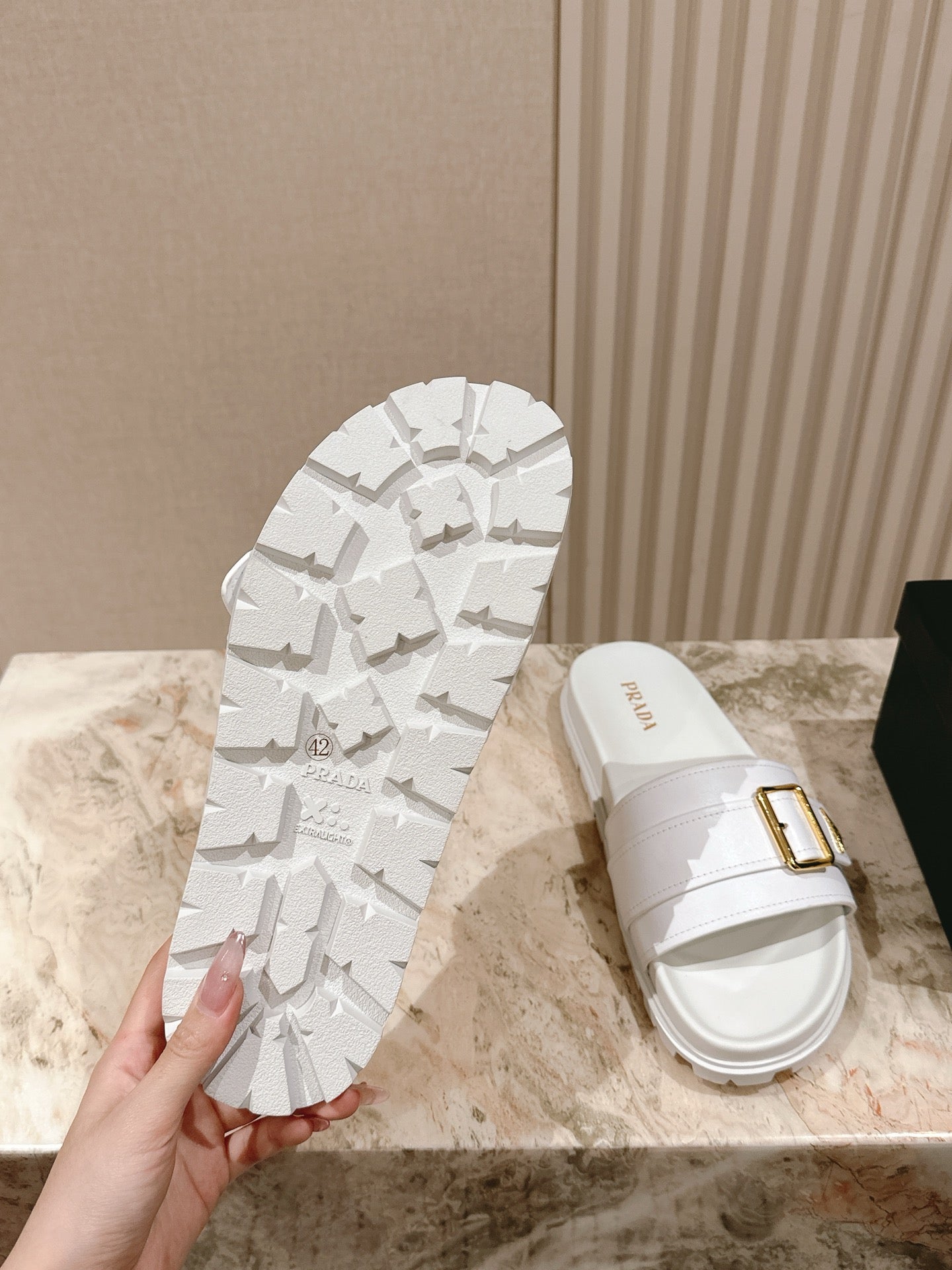 White Prada unisex slide sandal with patterned outsole and gold buckle