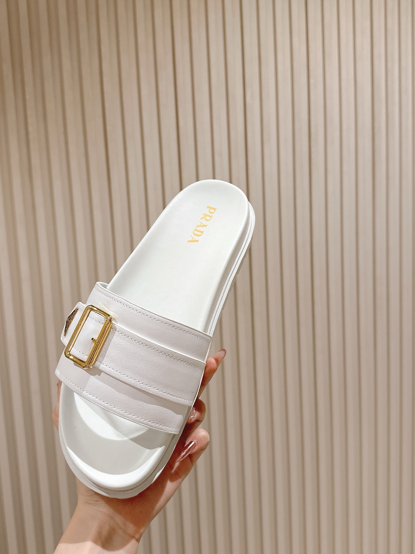 White Prada slide sandal with gold logo on footbed and gold buckle strap