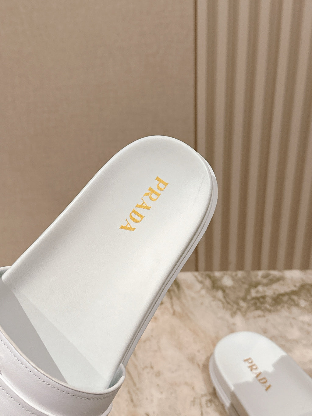 White Prada slide sandal with gold logo on footbed and side strap
