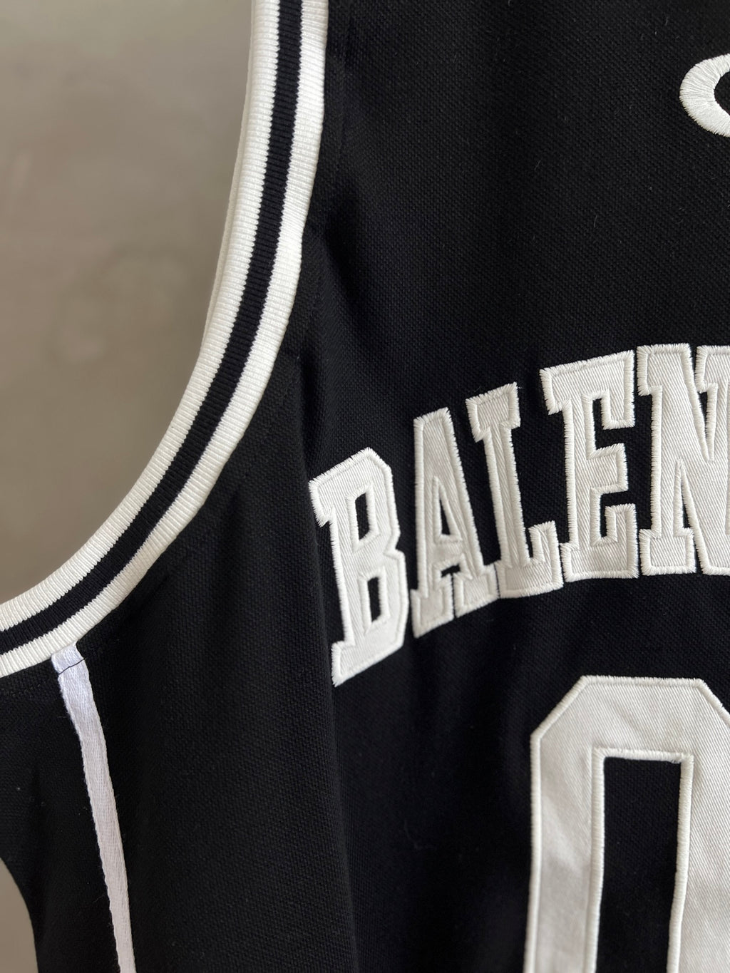 Black basketball jersey close-up with white Balenciaga lettering on the hem