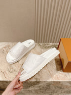 White slip-on slide sandals with embossed monogram pattern and thick sole