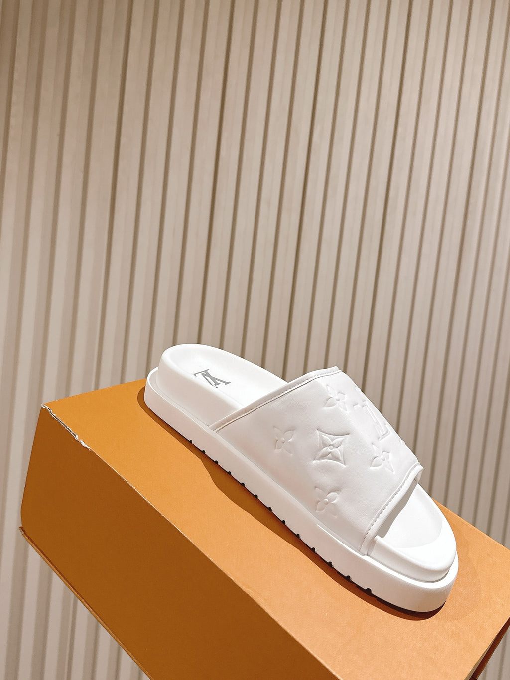 White monogram slide sandals with open toe and embossed pattern on strap