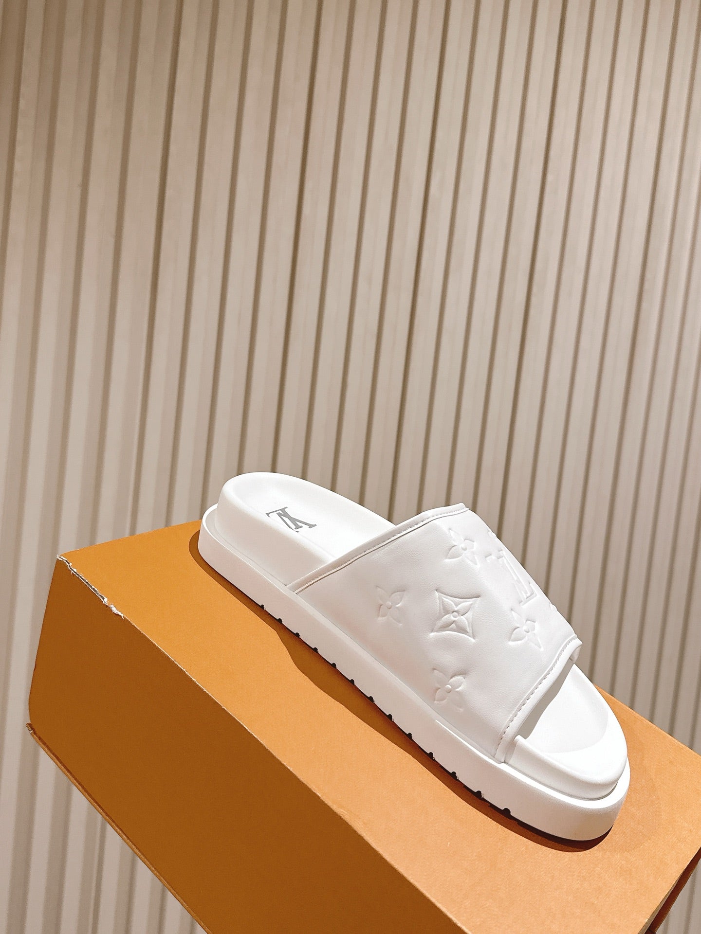 White monogram slide sandals with open toe and embossed pattern on strap