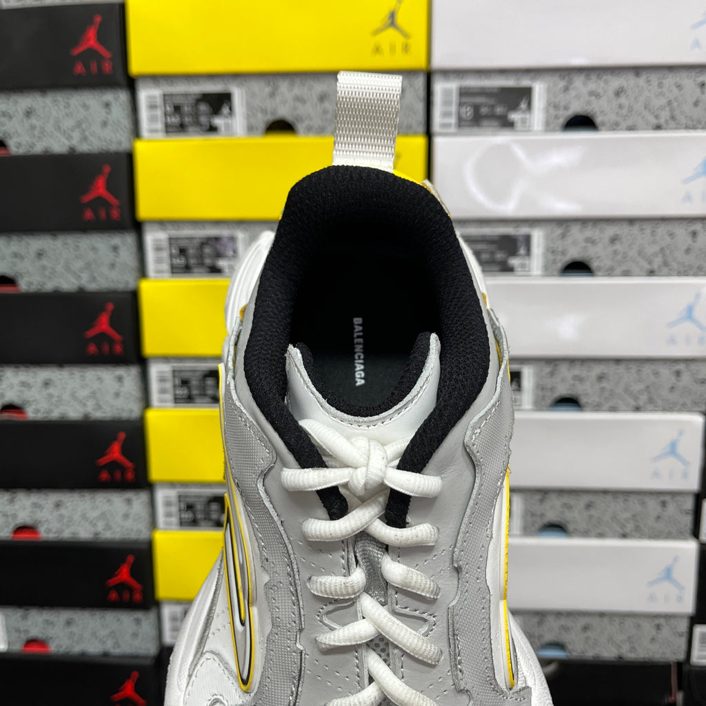 White unisex sneaker with black heel lining and yellow side stripe, rear view