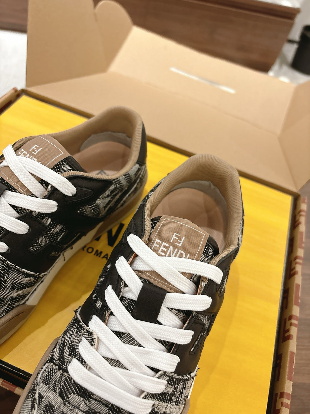 Fendi sneakers close-up in box, black/white logo knit, white laces, beige rubber sole.