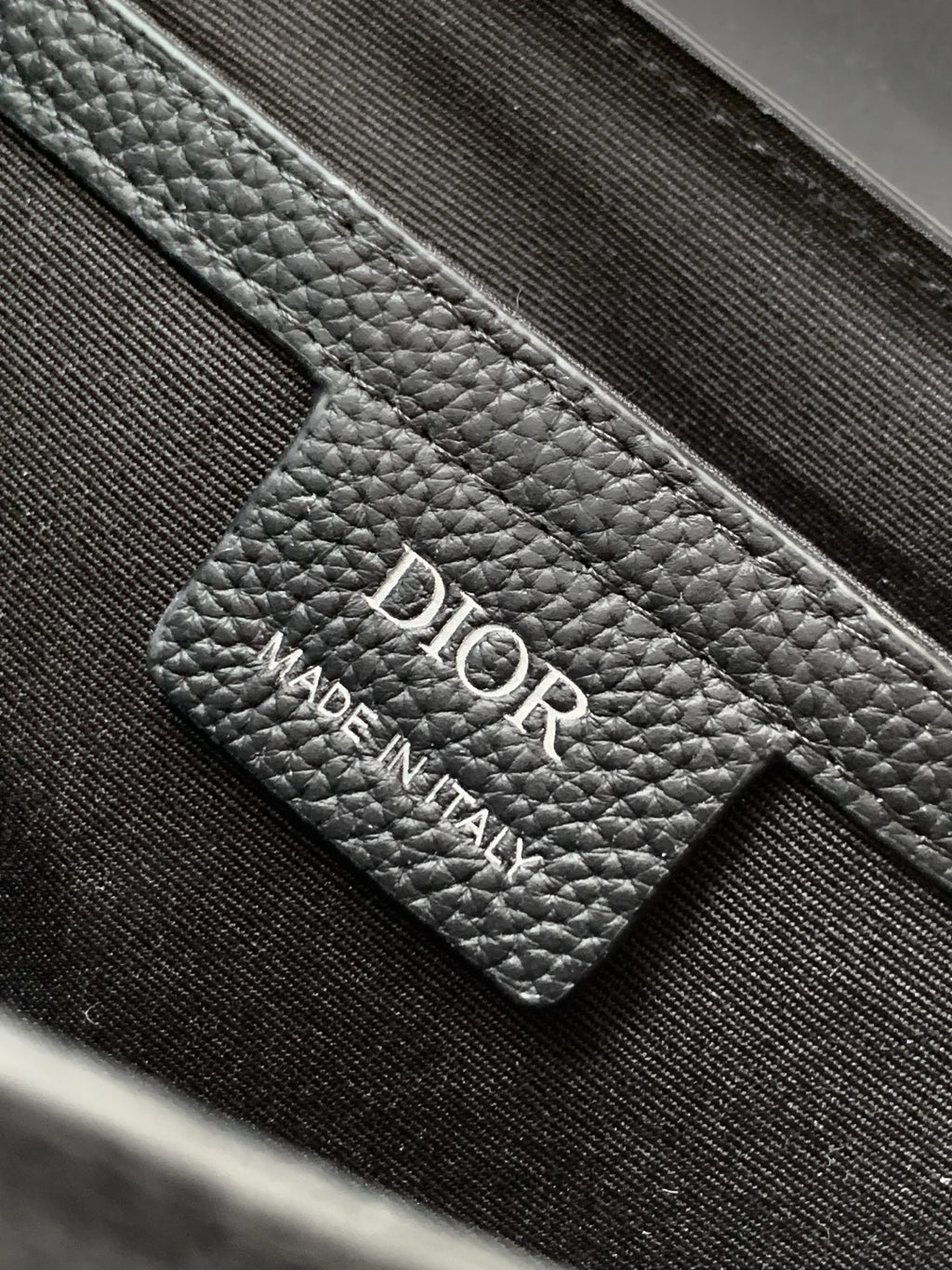 Dior leather label reading "DIO R" and "MADE IN ITALY" on dark fabric