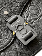 Close-up of Dior metal emblem charm on dark leather flap with belt-style buckle
