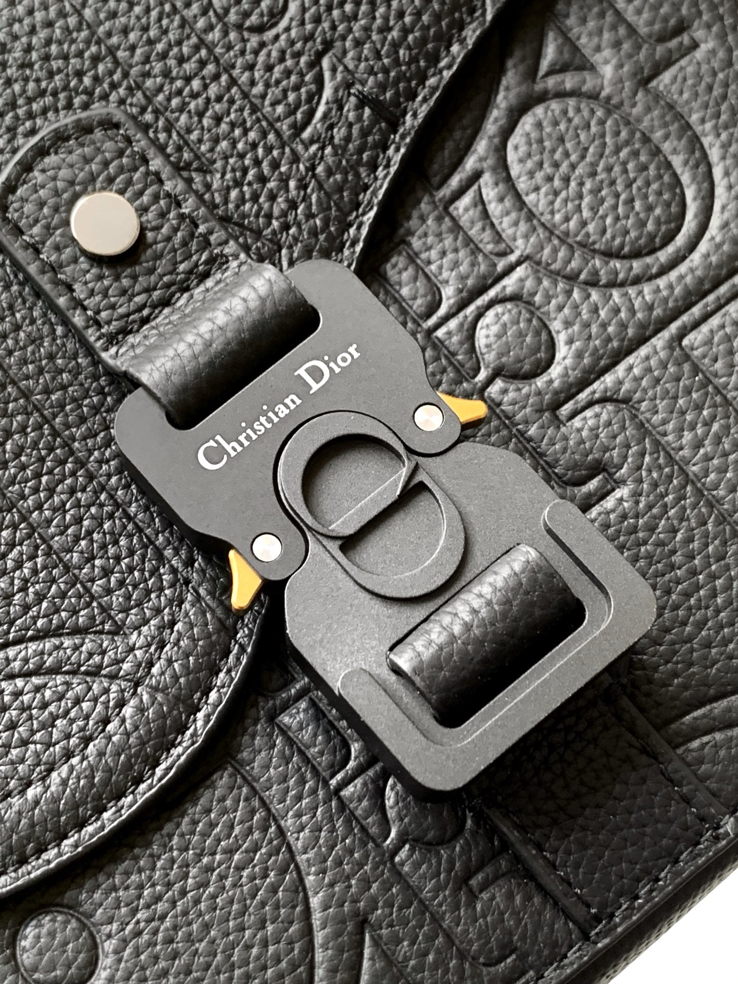 Close-up of Dior metal emblem charm on dark leather flap with belt-style buckle