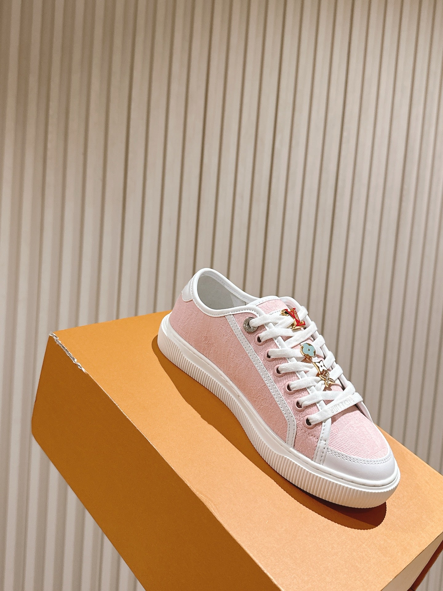 Pink and white low-top sneakers on a tan box, with white laces and side logo