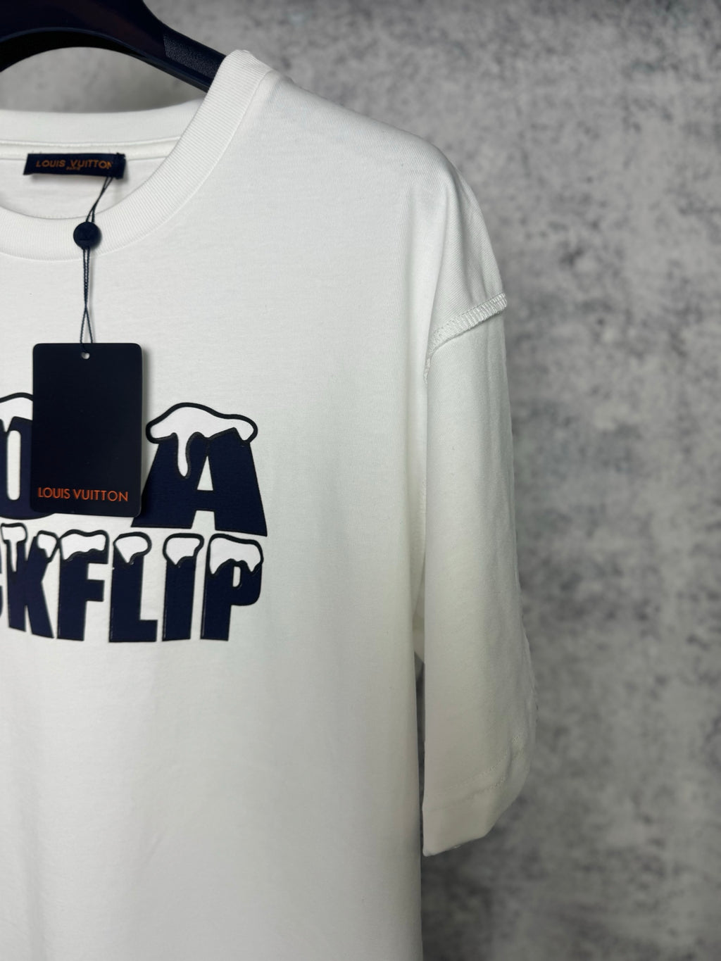 White T-shirt angled view with partial navy "DO A KICKFLIP" graphic and hanging tag