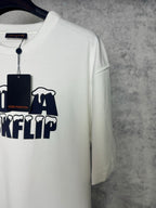 White T-shirt angled view with partial navy "DO A KICKFLIP" graphic and hanging tag