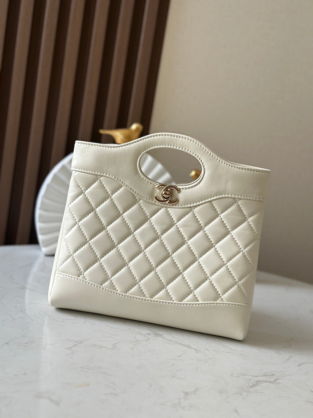 Chanel quilted cream handbag with oval handle, stitched edges, and gold-tone hardware