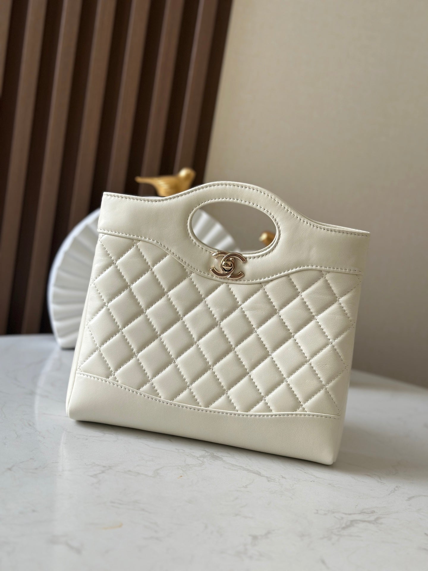 Chanel quilted cream handbag with oval handle, stitched edges, and gold-tone hardware