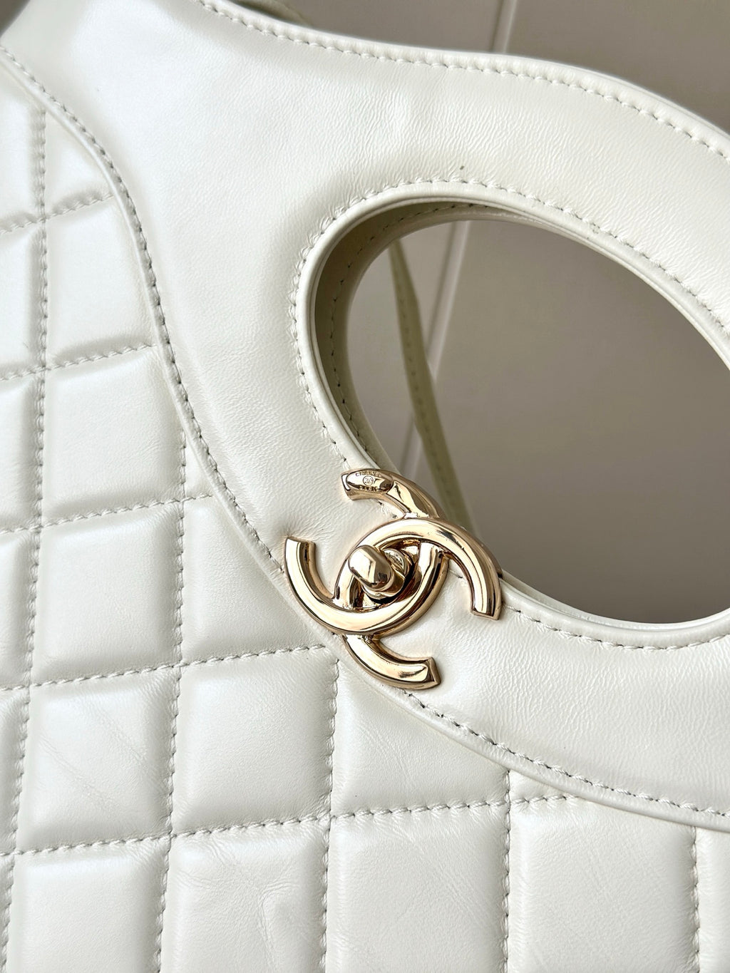 Chanel CC logo clasp on white quilted leather handbag, close-up.