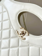 Chanel CC logo clasp on white quilted leather handbag, close-up.