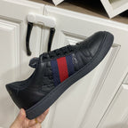 Gucci unisex lace-up sneakers, black leather with wide red-blue web stripe on side.
