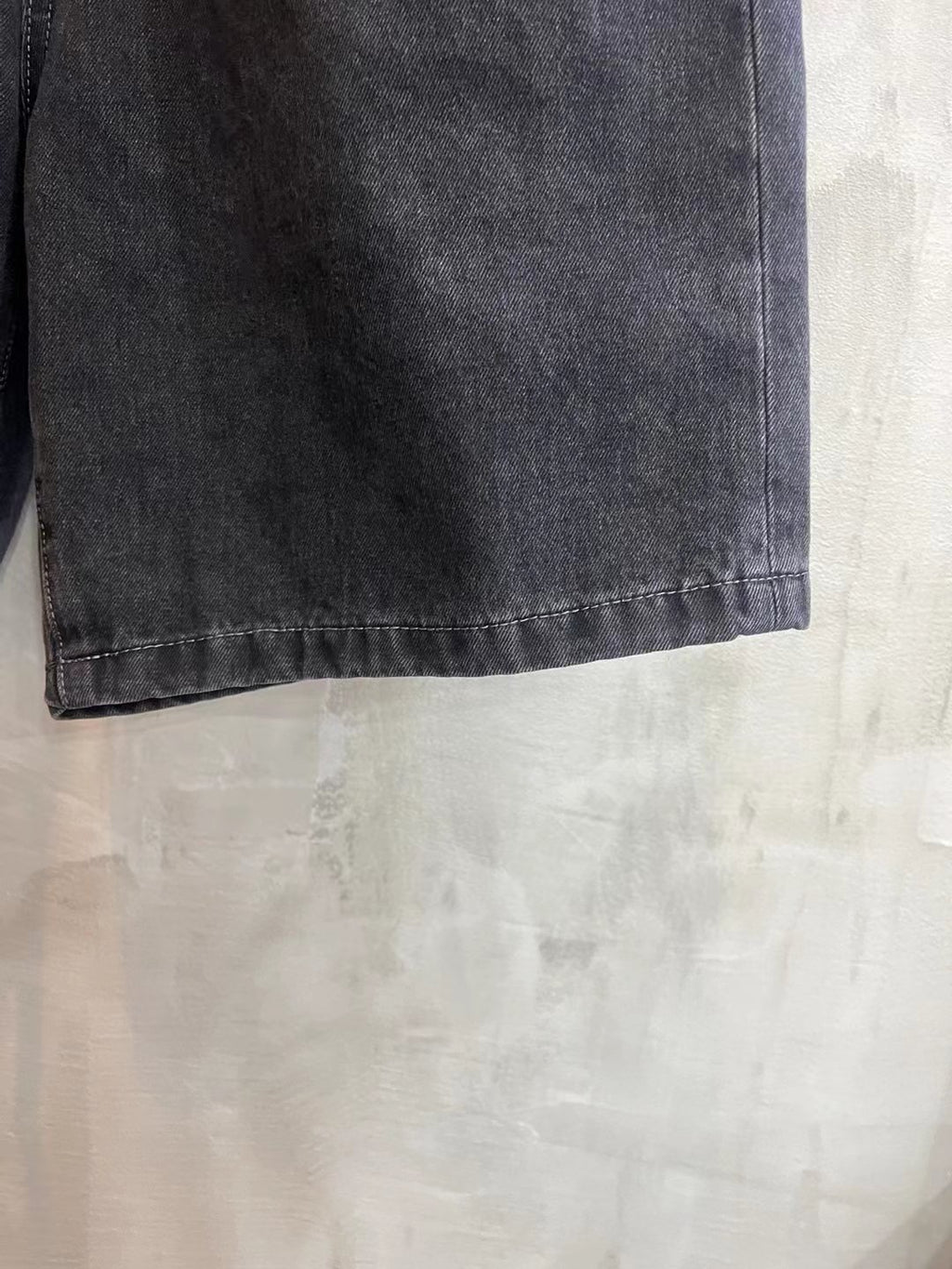 Dark wash denim shorts fabric and hem detail, showing straight side seam and stitching