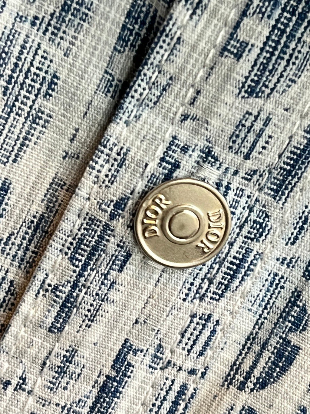 Round gold-tone logo button on blue-and-white patterned shirt placket