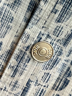 Round gold-tone logo button on blue-and-white patterned shirt placket