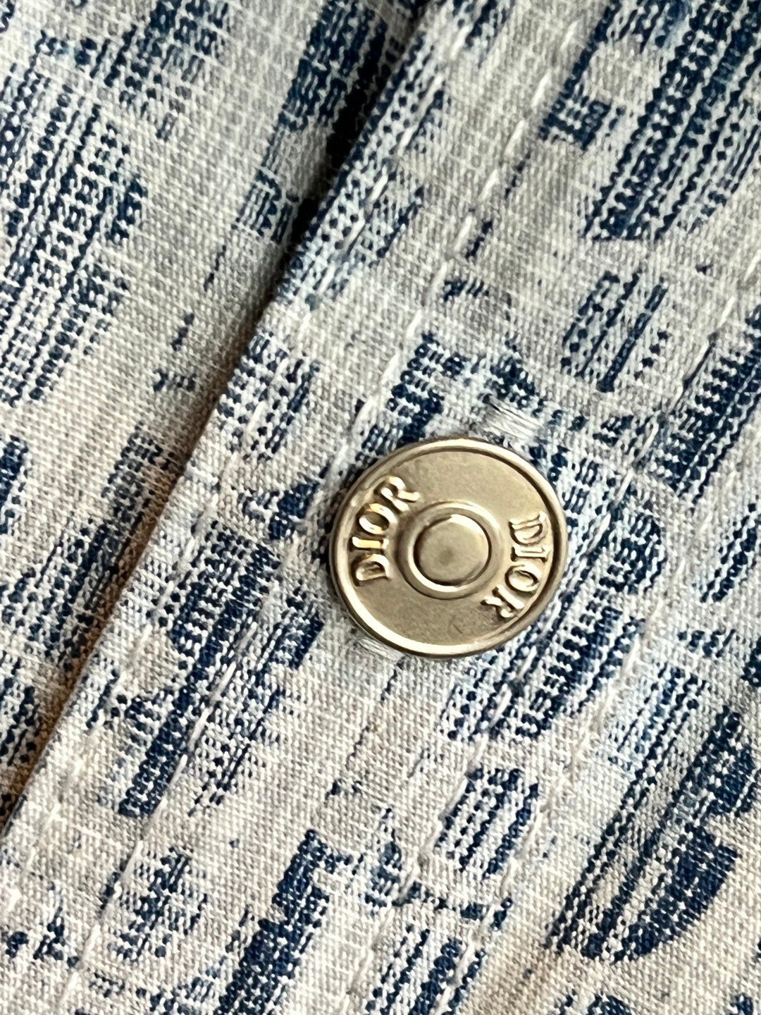 Round gold-tone logo button on blue-and-white patterned shirt placket