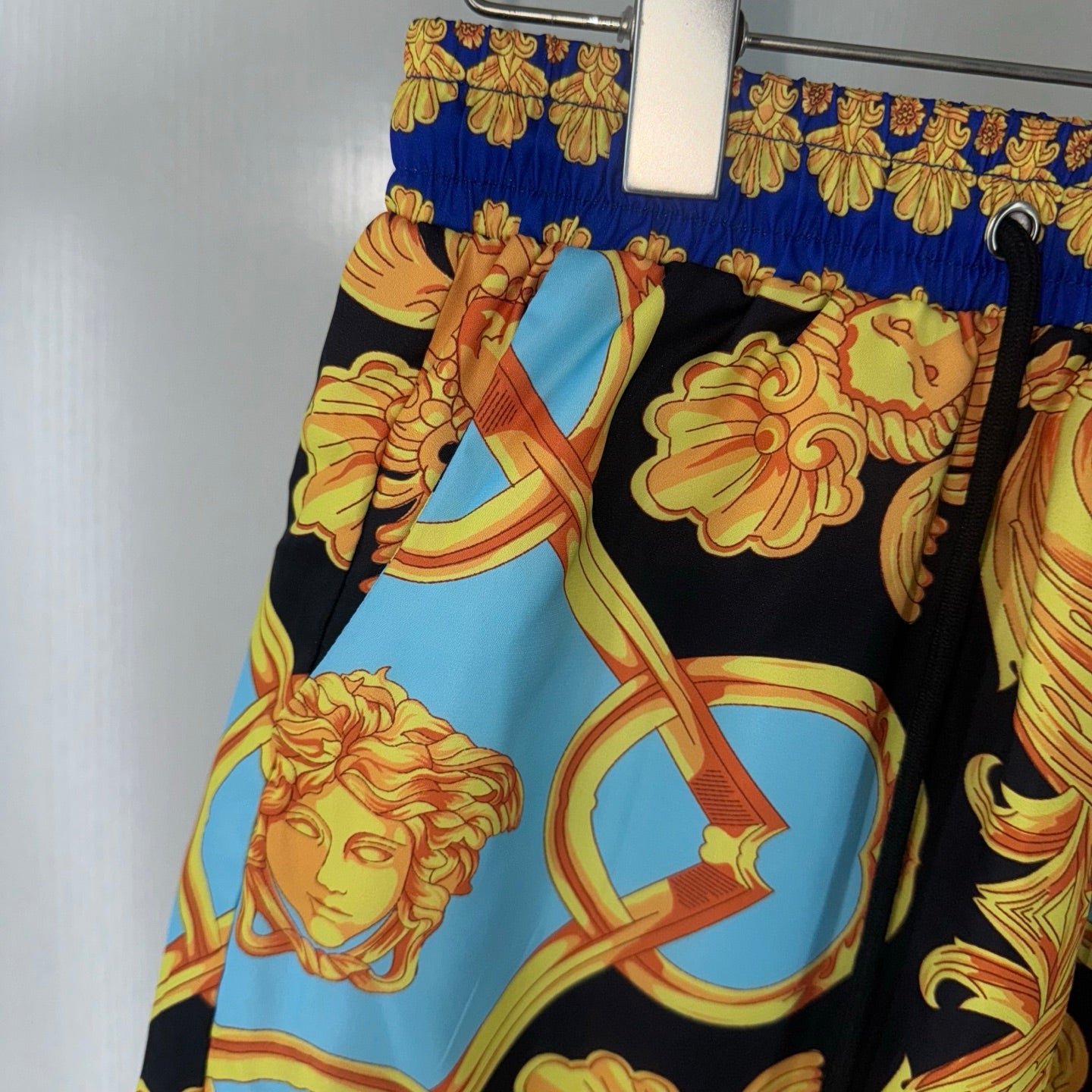 Versace shorts side view showing black base with light blue figure medallion print