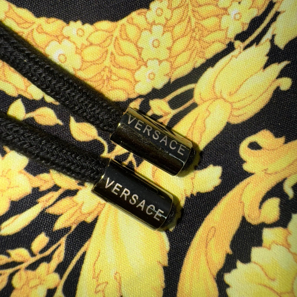 “VERSACE” brand tags on yellow floral print fabric with dark trim on shorts