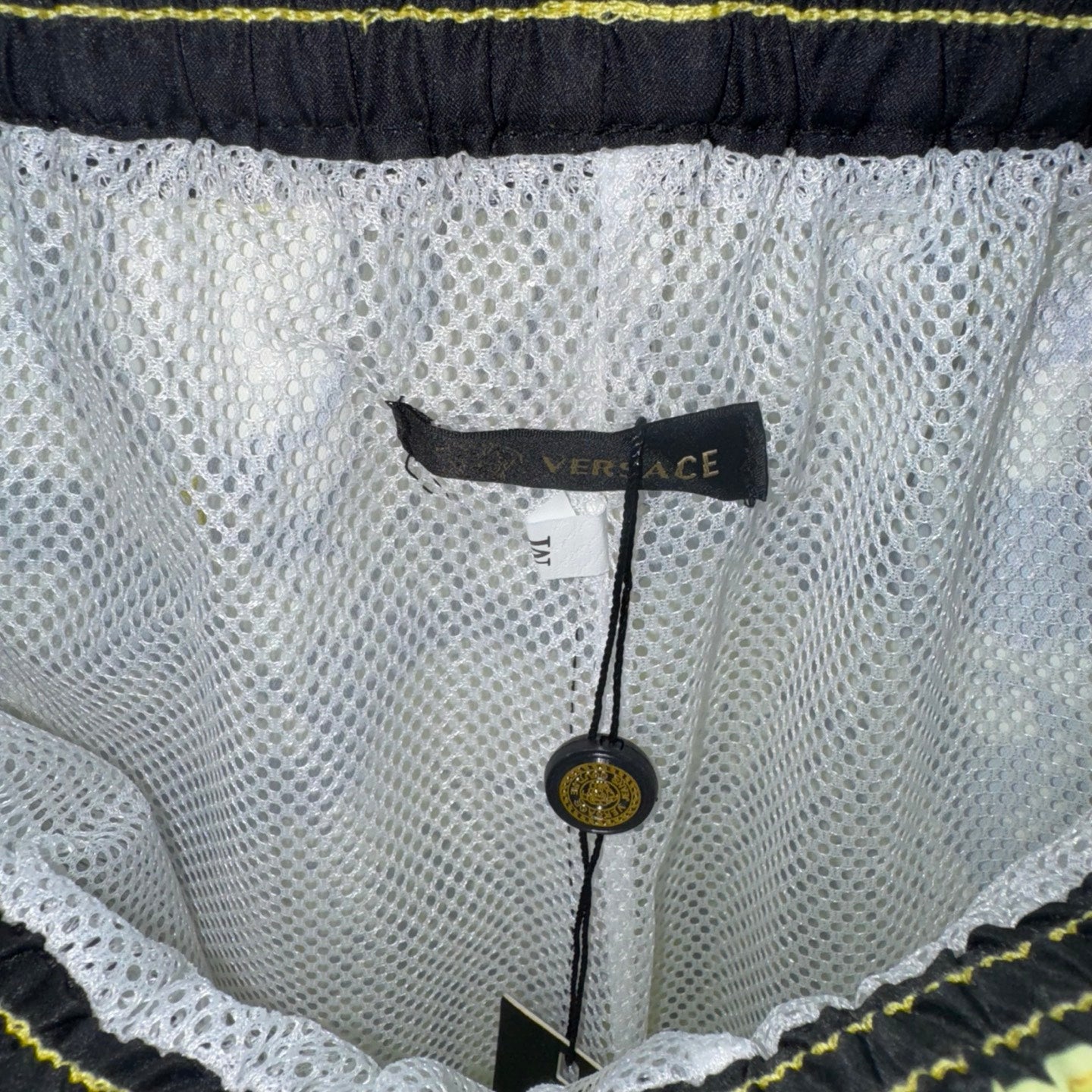 White mesh shorts with “VERSACE” label at waistband, textured fabric and scalloped trim