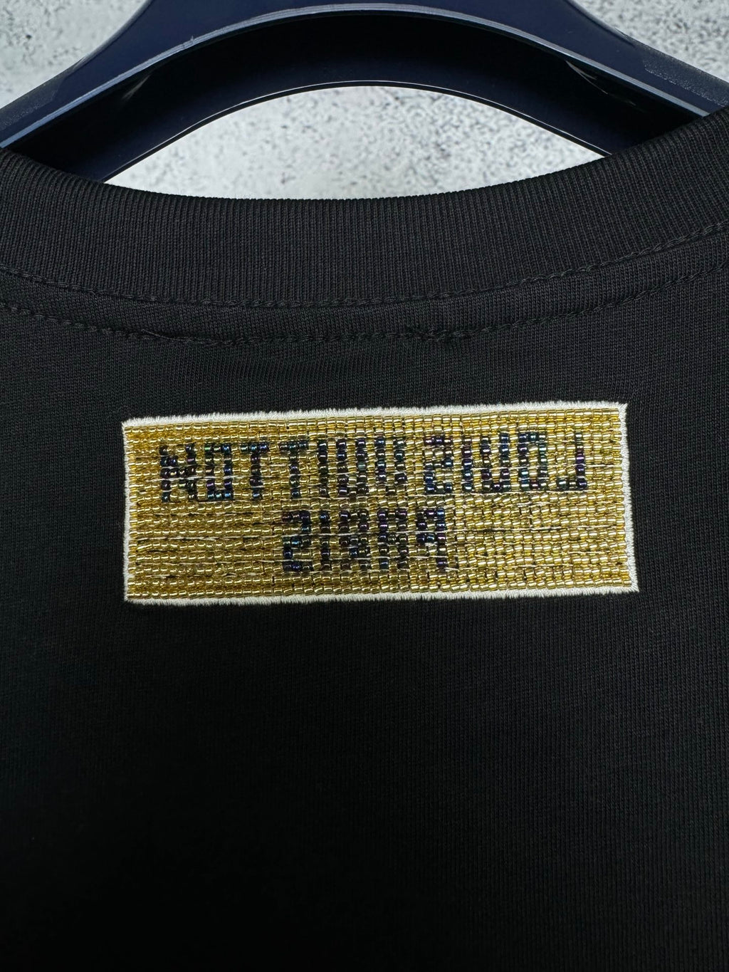 Close-up of black T-shirt neck label with yellow text and blue stripe