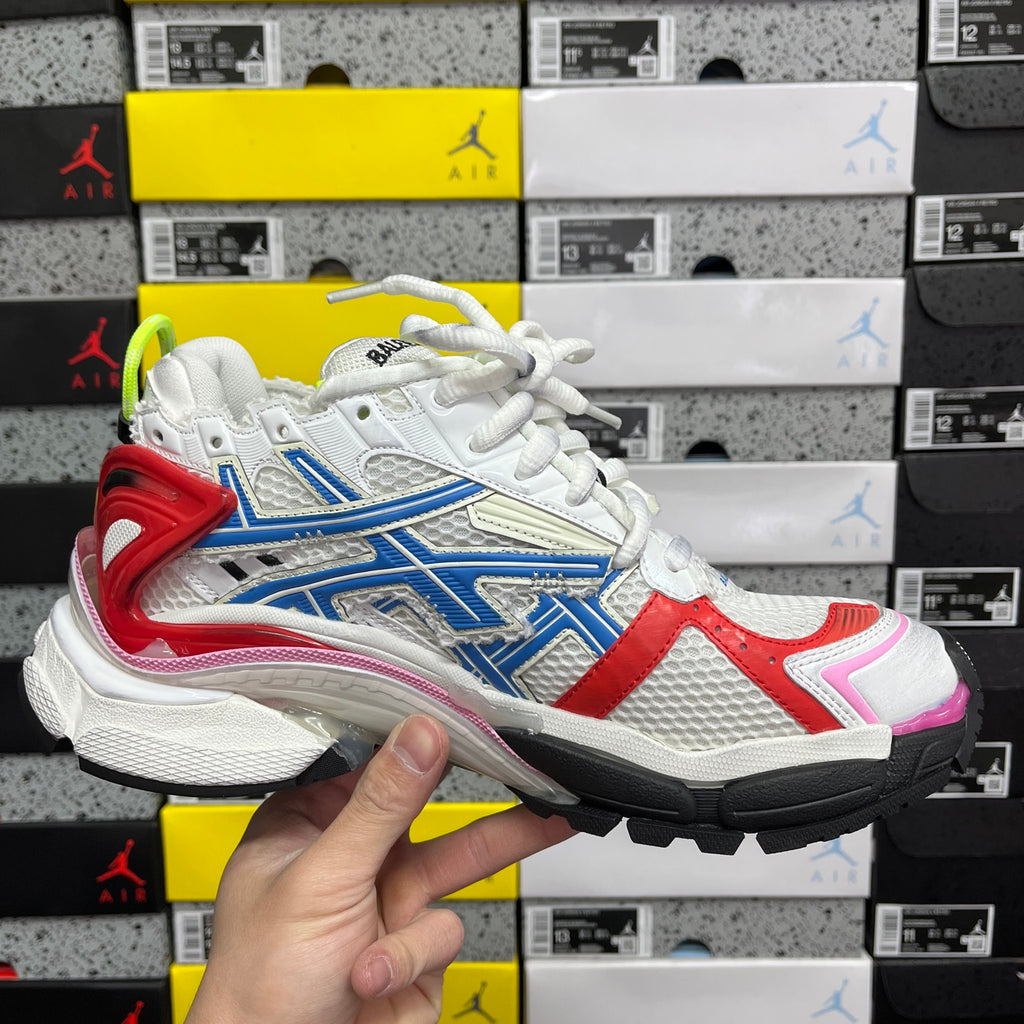 Unisex sneaker angled side view with white upper, blue and red panels, pink toe accent
