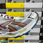 Silver sneaker side with orange-brown stripe, blue outsole edge, and purple laces