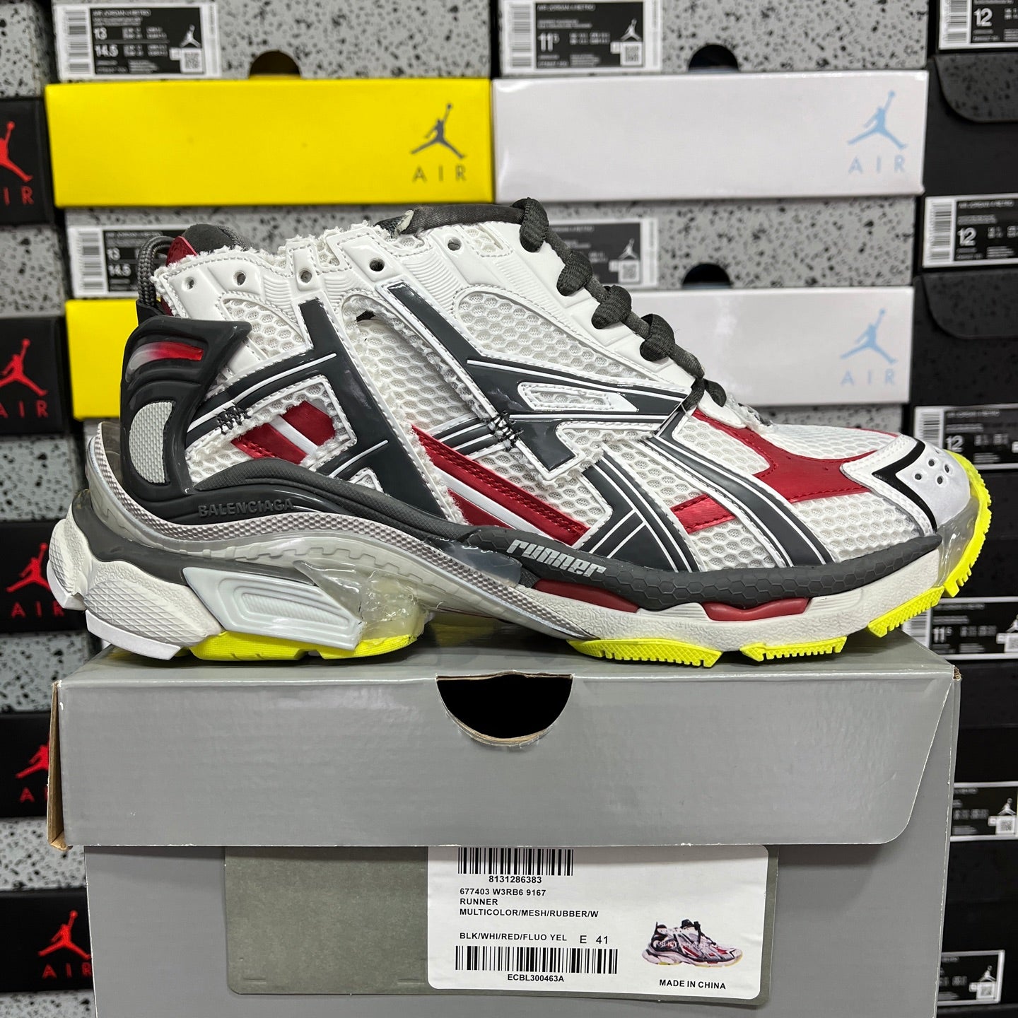 White, red, and black sneaker on box, black laces, and textured yellow outsole