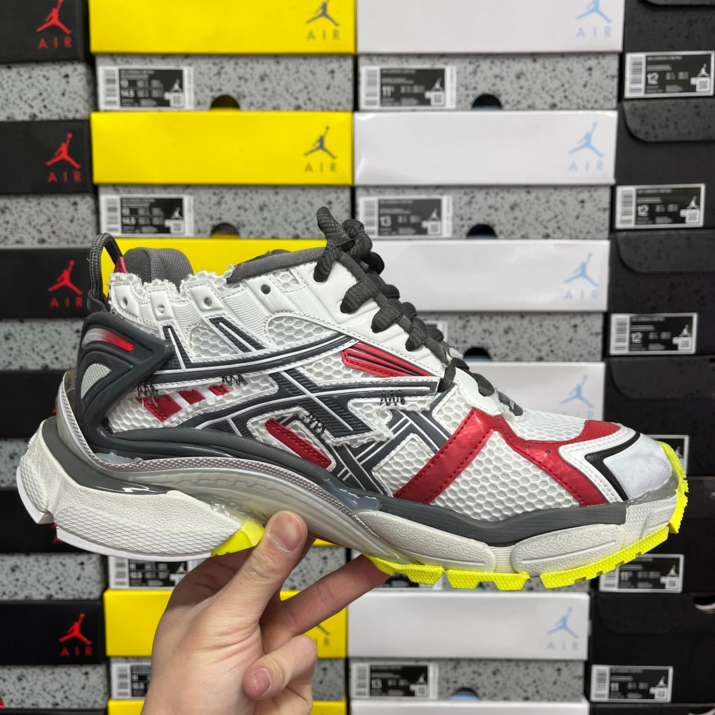 White, red, and black low-top sneaker with black laces and yellow outsole edge