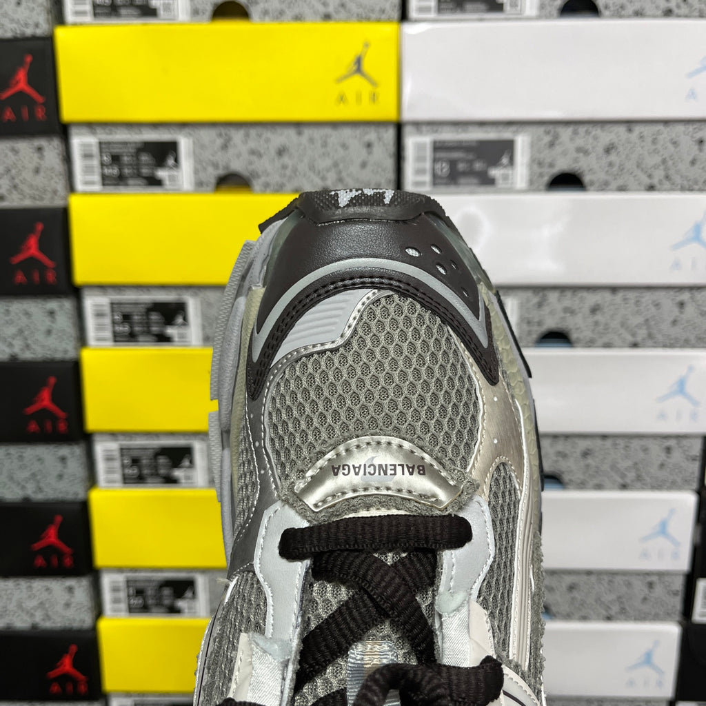Silver-gray sneaker heel panel with mesh texture and black lace near eyelets.